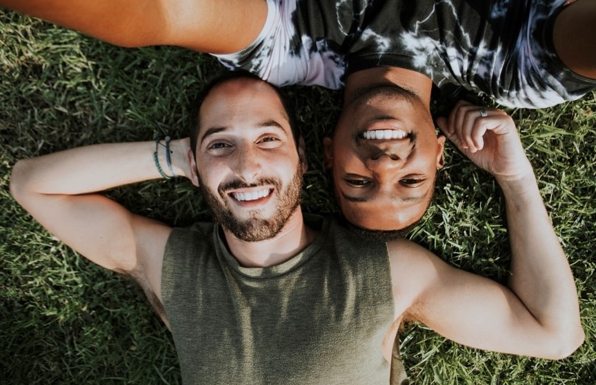 romance gay dans la nature avec un homme black et un caucasien allongés dans l'herbe verte souriants